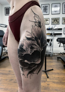 Tatouage d'une fleur noir et grise réaliste corps femme