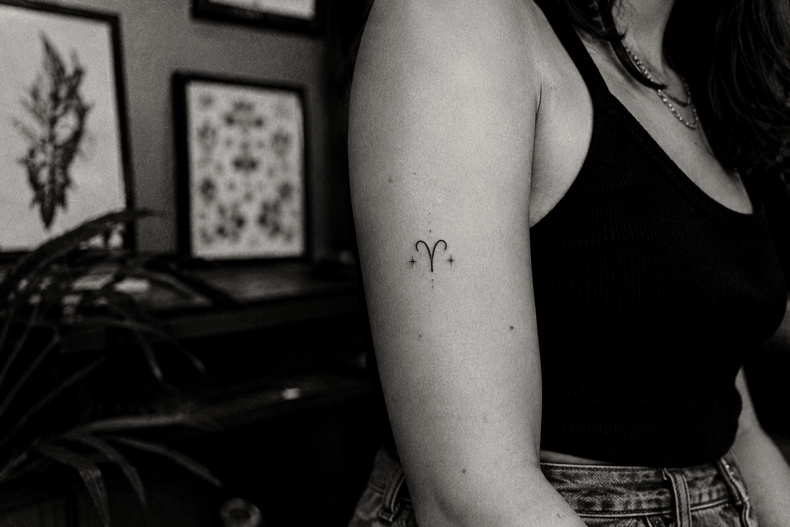 Petit tatouage du glyphe du Bélier entouré de deux étoiles sur le haut du bras d’une femme