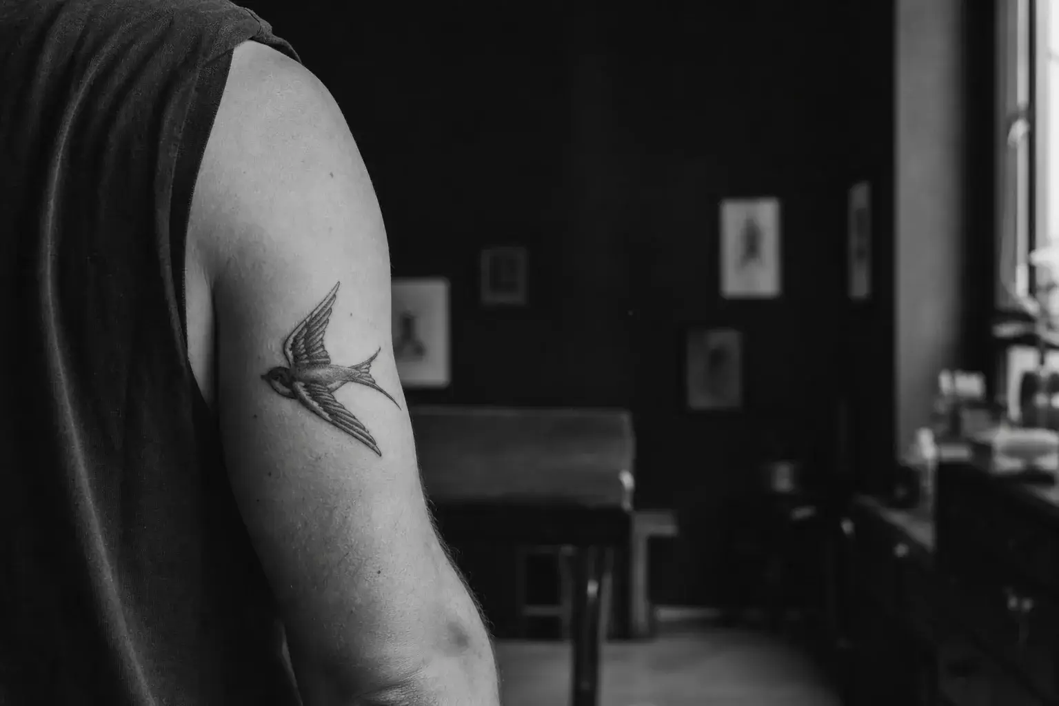 Tatouage d’hirondelle noir et gris sur le haut du bras