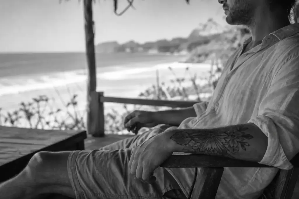 Personne tatouée assise à l’ombre face à la plage