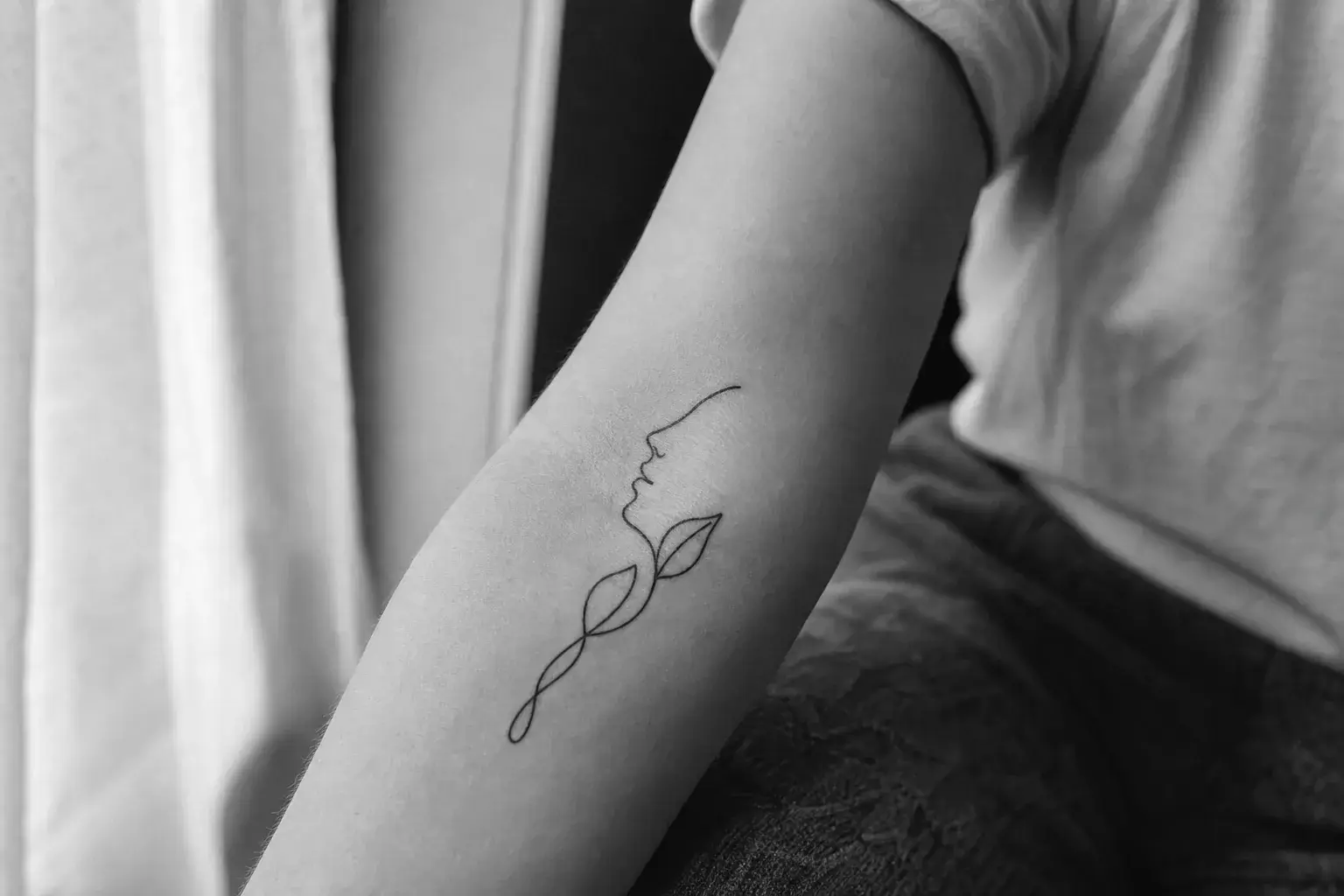 Tatouage One Line cicatrisé représentant un visage et des feuilles sur l'avant-bras
