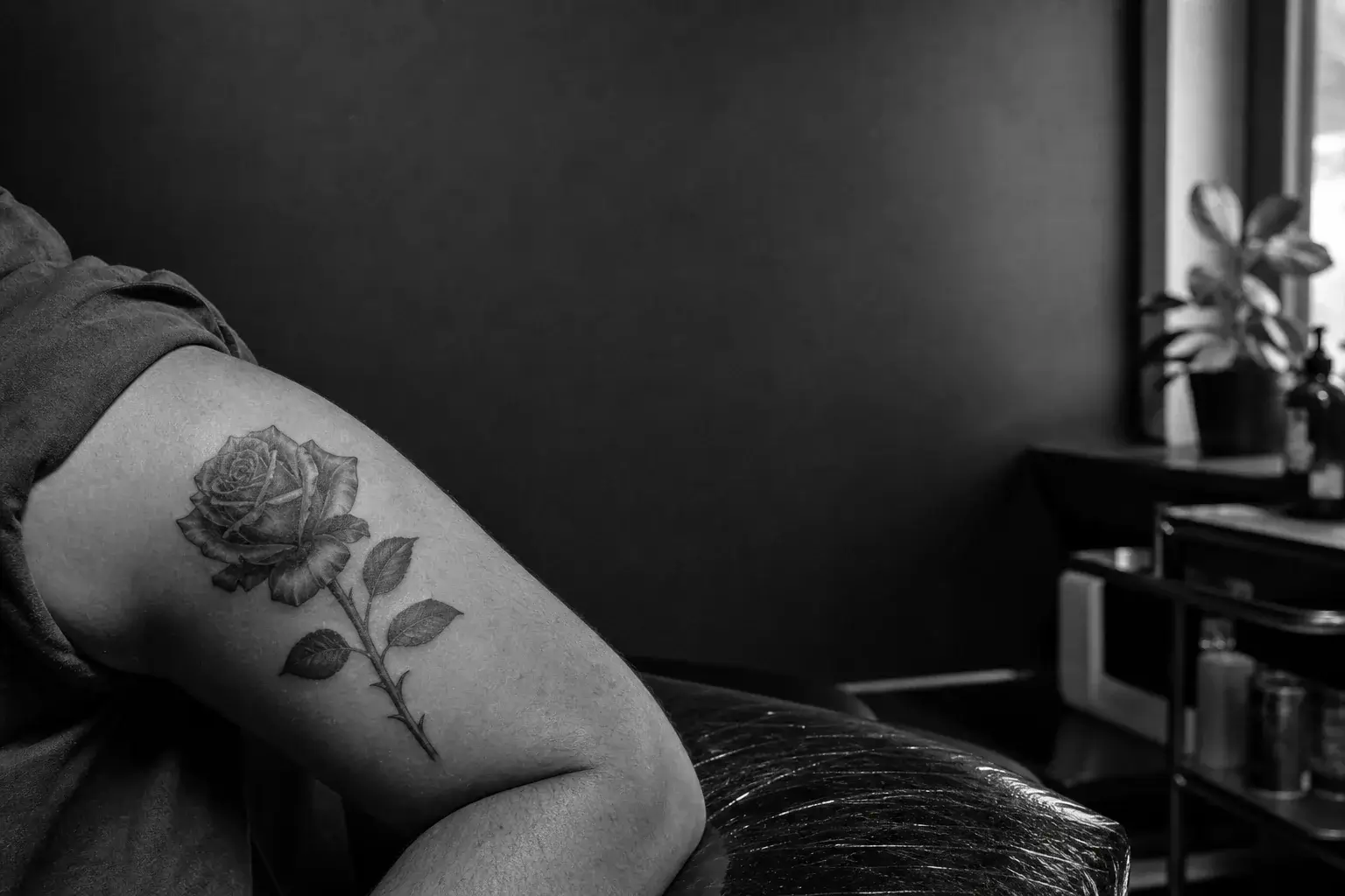 Rose avec tige et épines tatouée en noir et gris sur le haut du bras